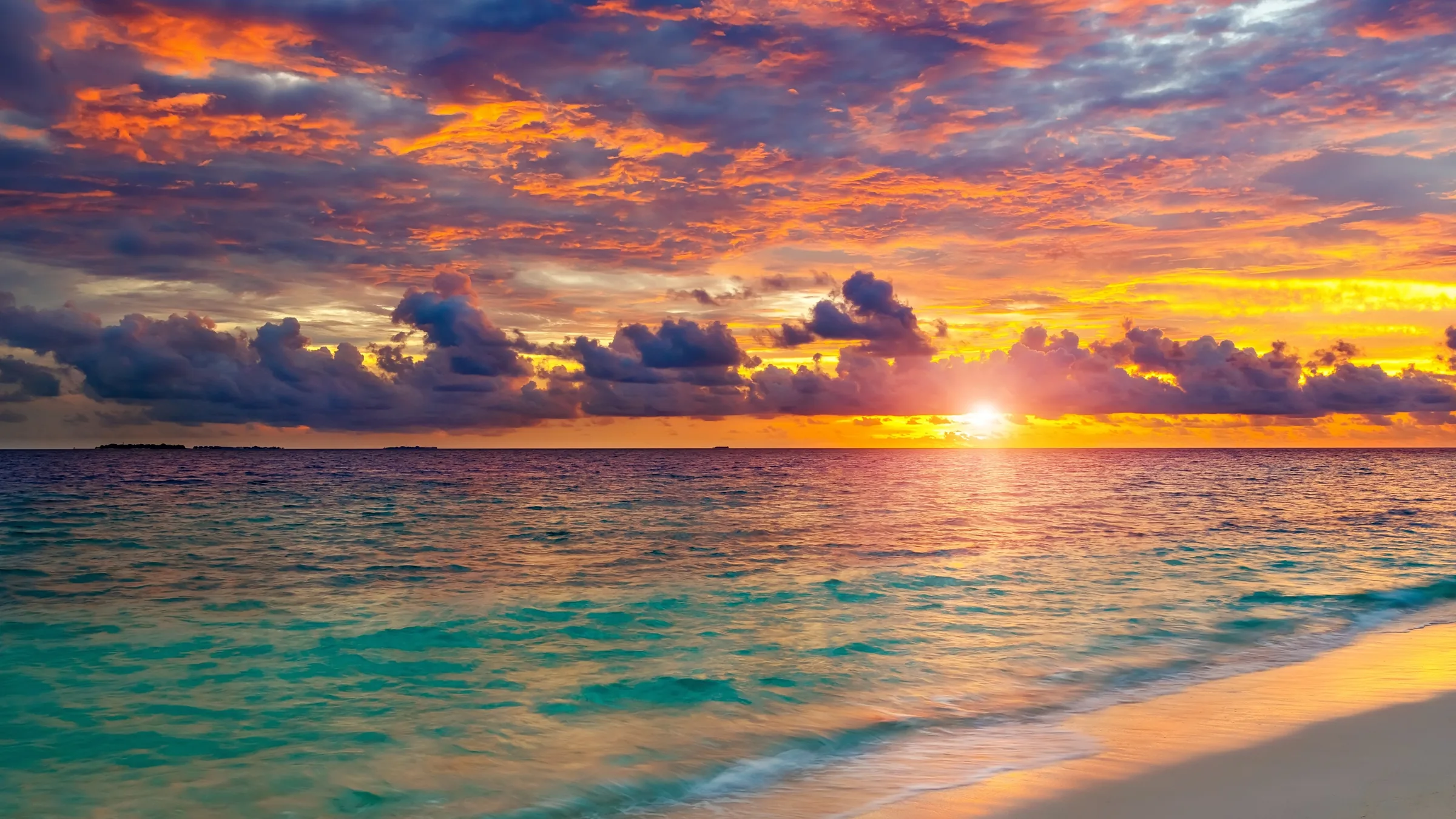 Vibrant sunset over a tropical beach with turquoise water and golden sand.